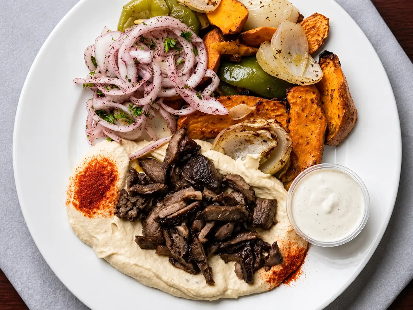 Plate with hummus, shawarma meat, pickled onions, and roasted vegetables