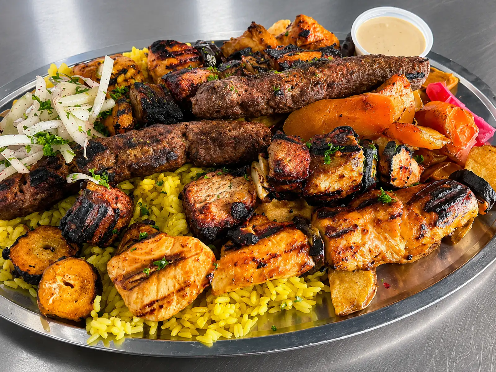 Platter of grilled meats, yellow rice, roasted potatoes, and sauce